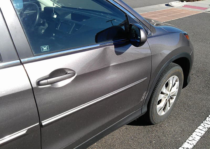 Before: a grey SUV's driver door with a dent below the window.