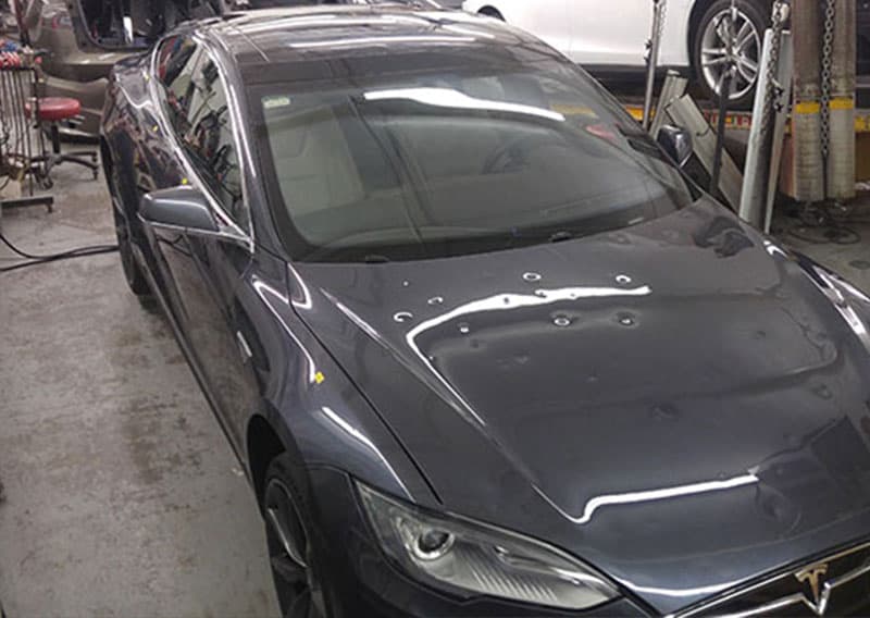 Hail dents across the hood of a dark Tesla Model S in the Caropractor shop.